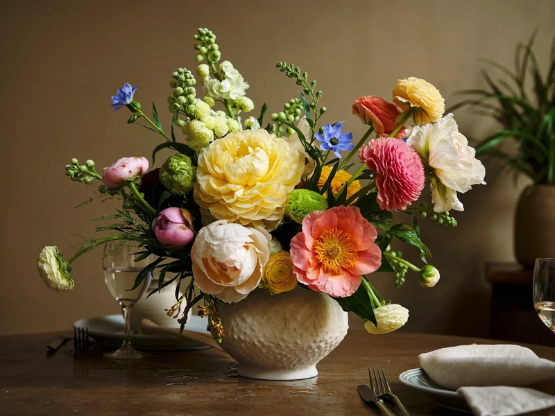 Lavt blomsterarrangement i stentøjsvase på et dækket spisebord